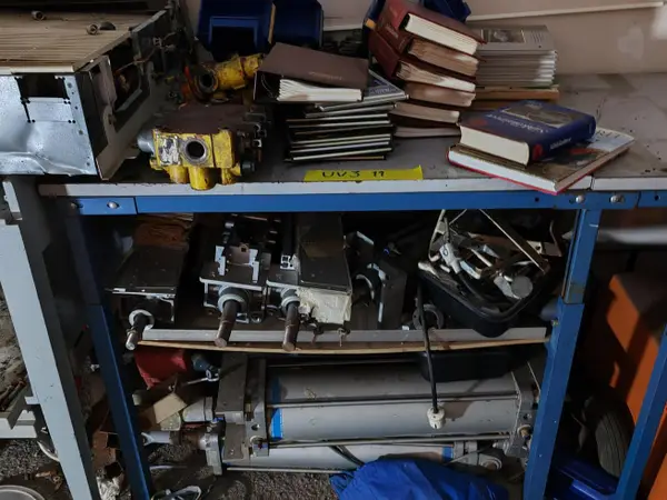 Työpöydän päällä ja hyllyillä olevat konepaja tarvikkeet ja opaskirjat. nro UV3 11